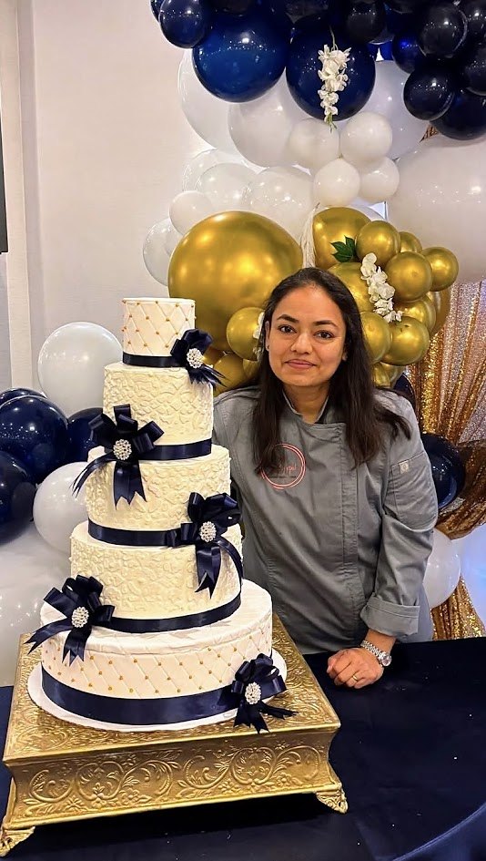 Ripal, cake artist and owner of Cakes by Ripal, beside a five-tier white, navy and gold egg-free wedding cake