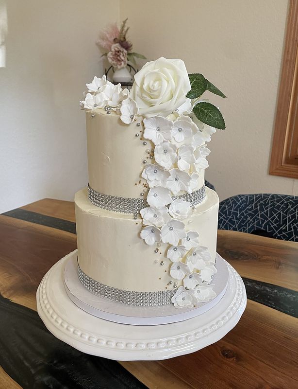 Two-tier white wedding cake with a cascade of handmade white sugar flowers and a crystal band